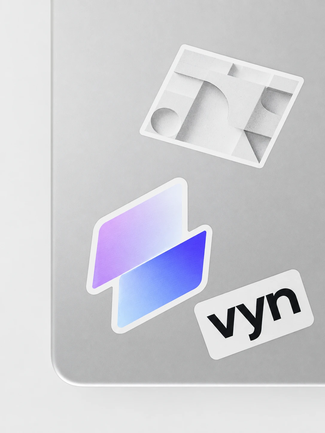Laptop with three VYN stickers: the Fold symbol, the vyn wordmark and an architectural form study